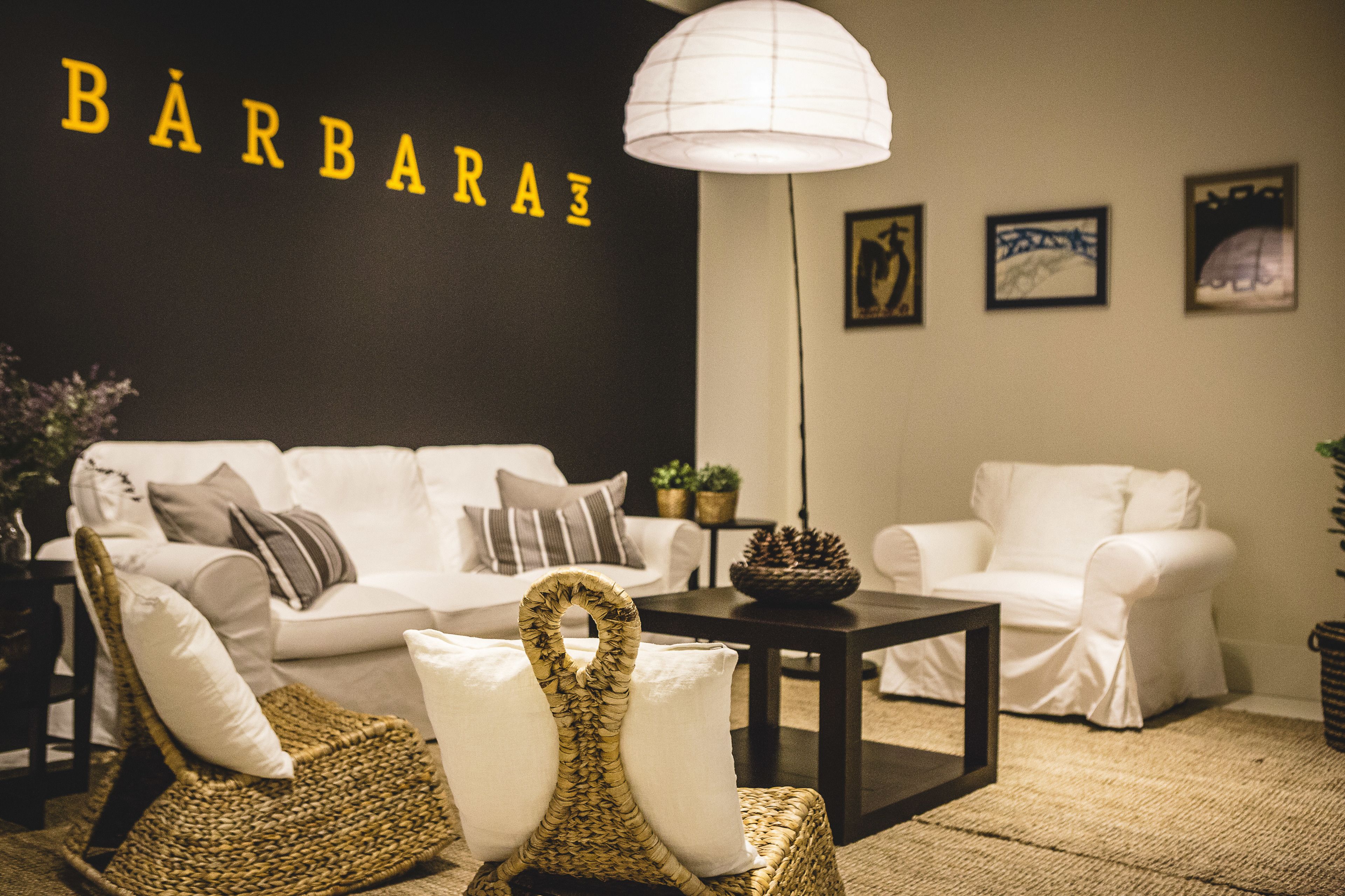 A modern living room with a white sofa, two wicker chairs, a coffee table, and a wall-mounted lamp.