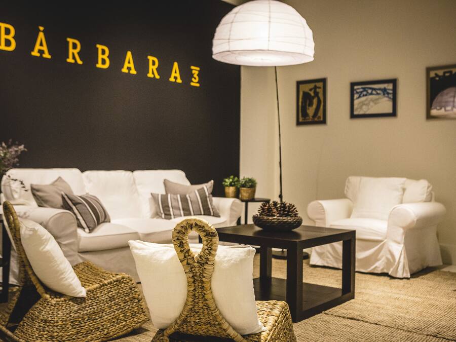 A modern living room with a white sofa, two wicker chairs, a coffee table, and a wall-mounted lamp.