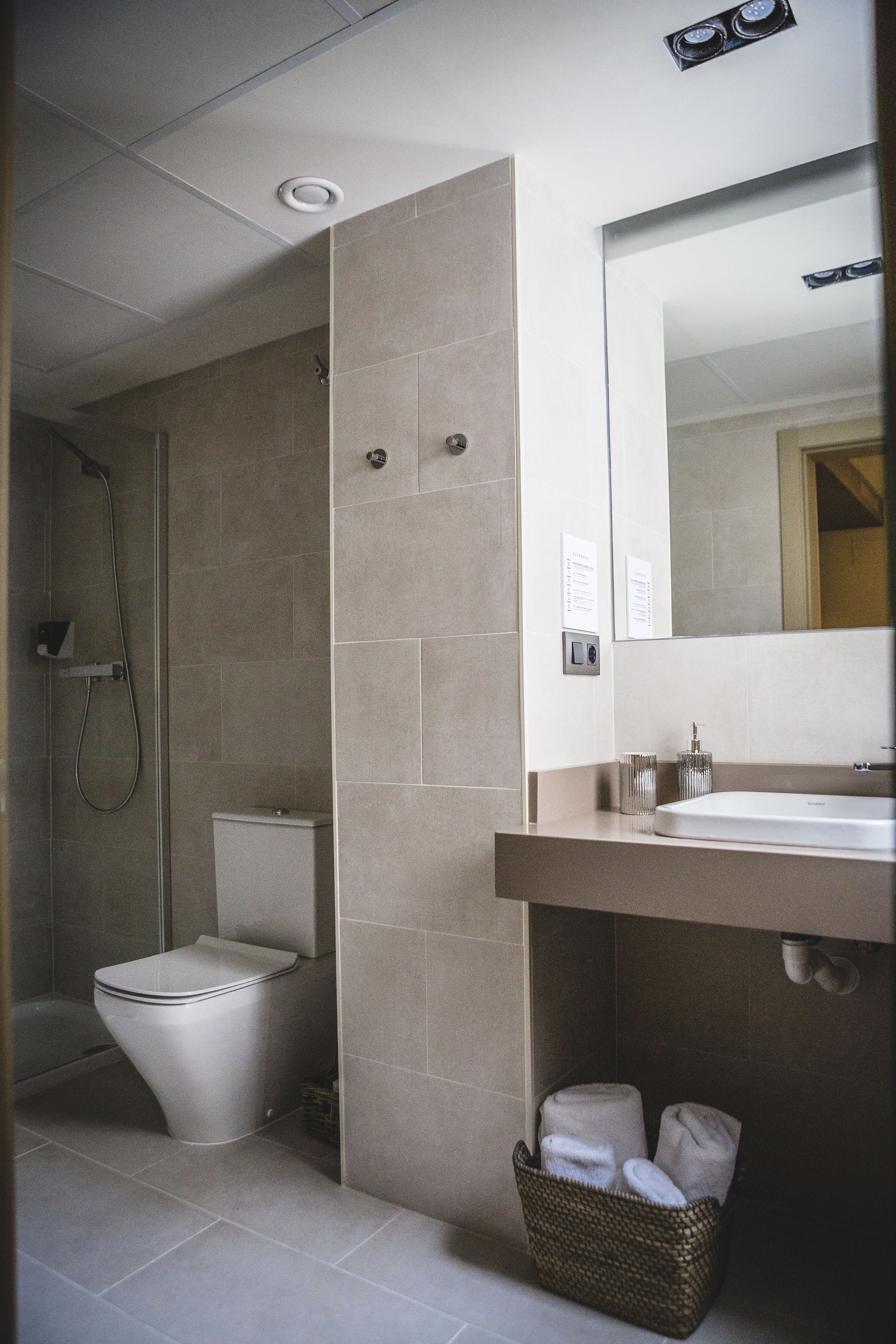 A modern bathroom with a shower, toilet, and a sink with a mirror above.