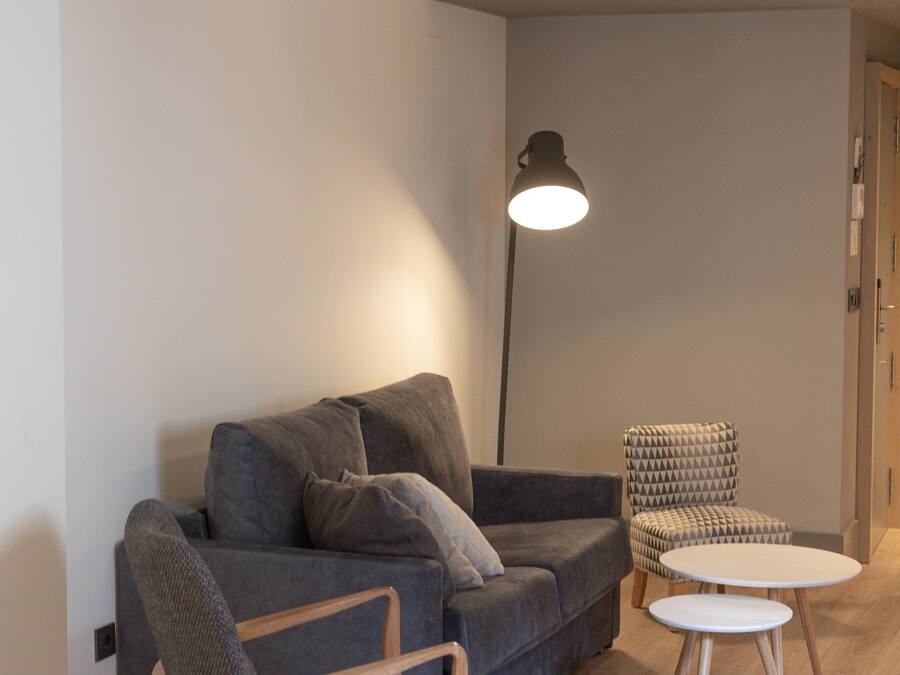 A modern living room with a grey sofa, a wooden armchair, a small round table, and a floor lamp.
