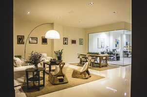 A modern living room with a sofa, two wicker chairs, a coffee table, and a dining area with a table and chairs.
