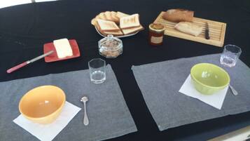 Una mesa con diversos alimentos y utensilios, como pan, un tarro de mermelada y un cuchillo.