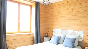 Ein Zimmer mit Holzwänden, einem Bett, einem Nachttisch und einem Fenster mit Vorhängen.