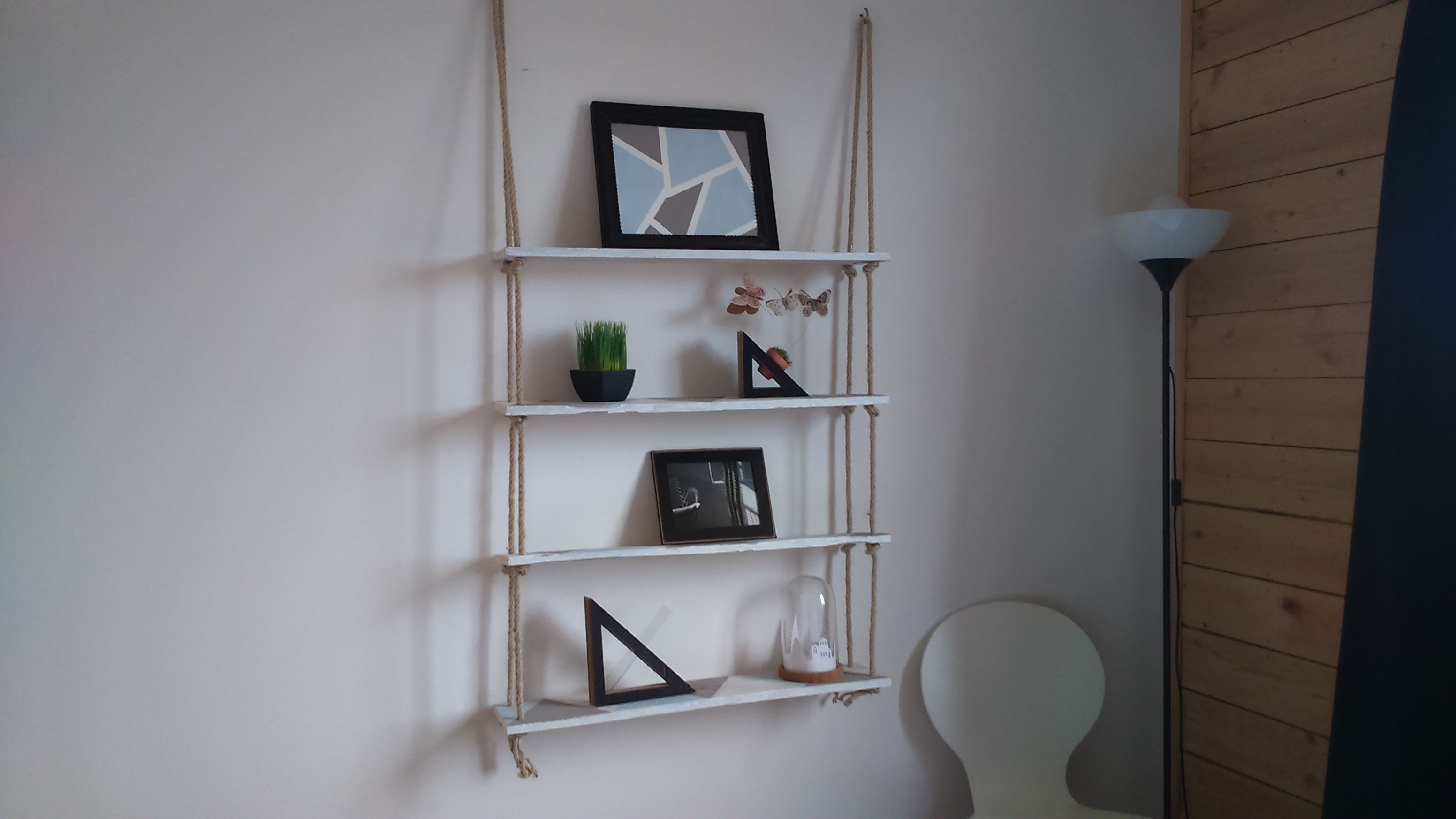 Una pared blanca con un estante de listones de madera que sostiene varios objetos decorativos.