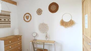 A room with a wooden dresser, a white desk with a chair, and wall decorations including a heart-shaped and a circular woven piece.
