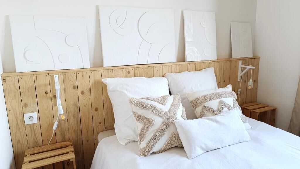 Un dormitorio con cabecera de madera, ropa de cama blanca y almohadas decorativas.