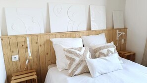 A bedroom with a wooden headboard, white bedding, and decorative pillows. - Maison Écologique en Paille (La Chapelle-Enchérie)
