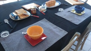 Ein Tisch gedeckt mit Brot, Butter, Marmelade, einem Messer, einer Schüssel und einem Löffel sowie einem Glas.