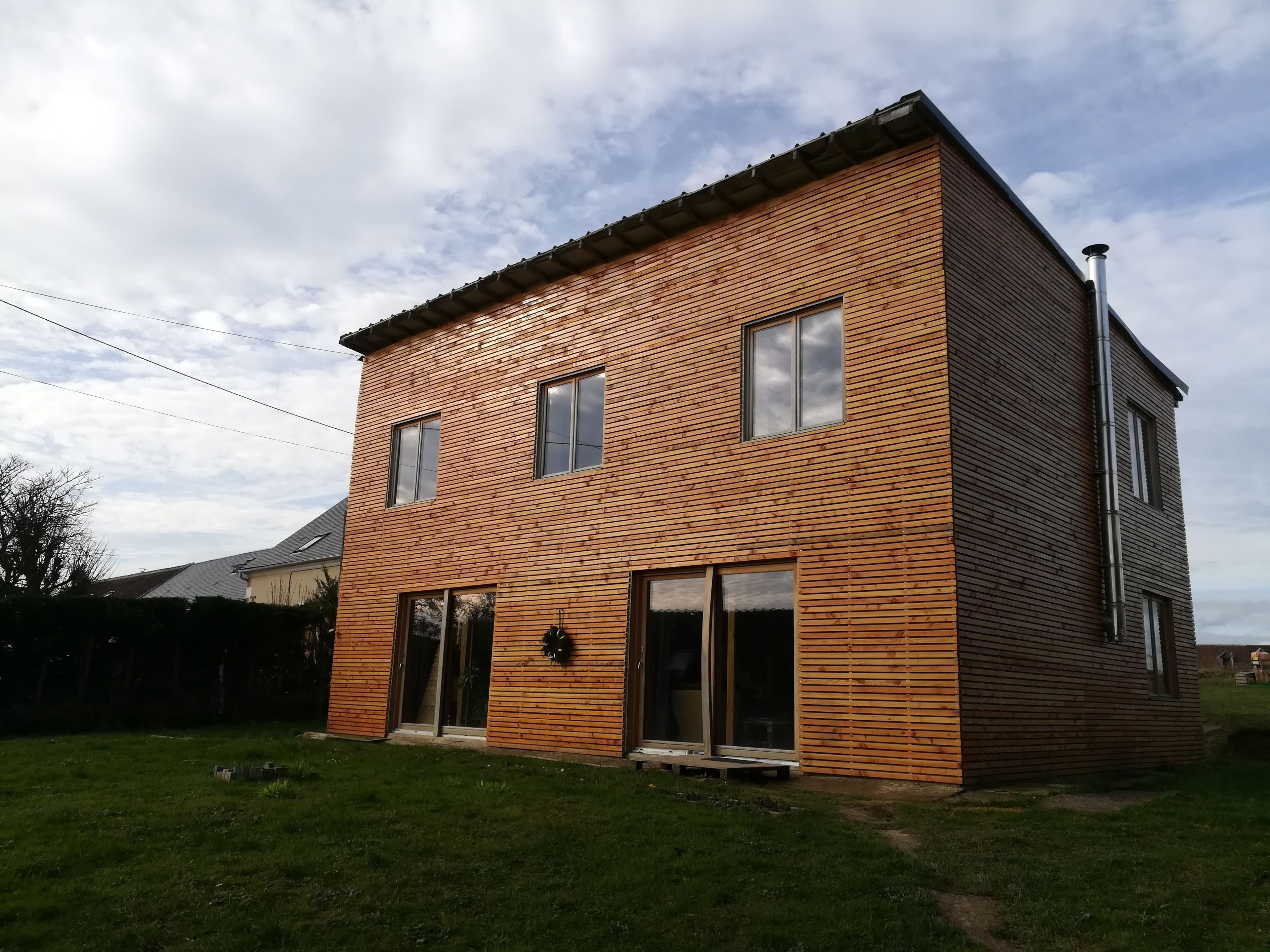 Una casa de dos pisos con fachada de madera, ventanas grandes y una chimenea visible.