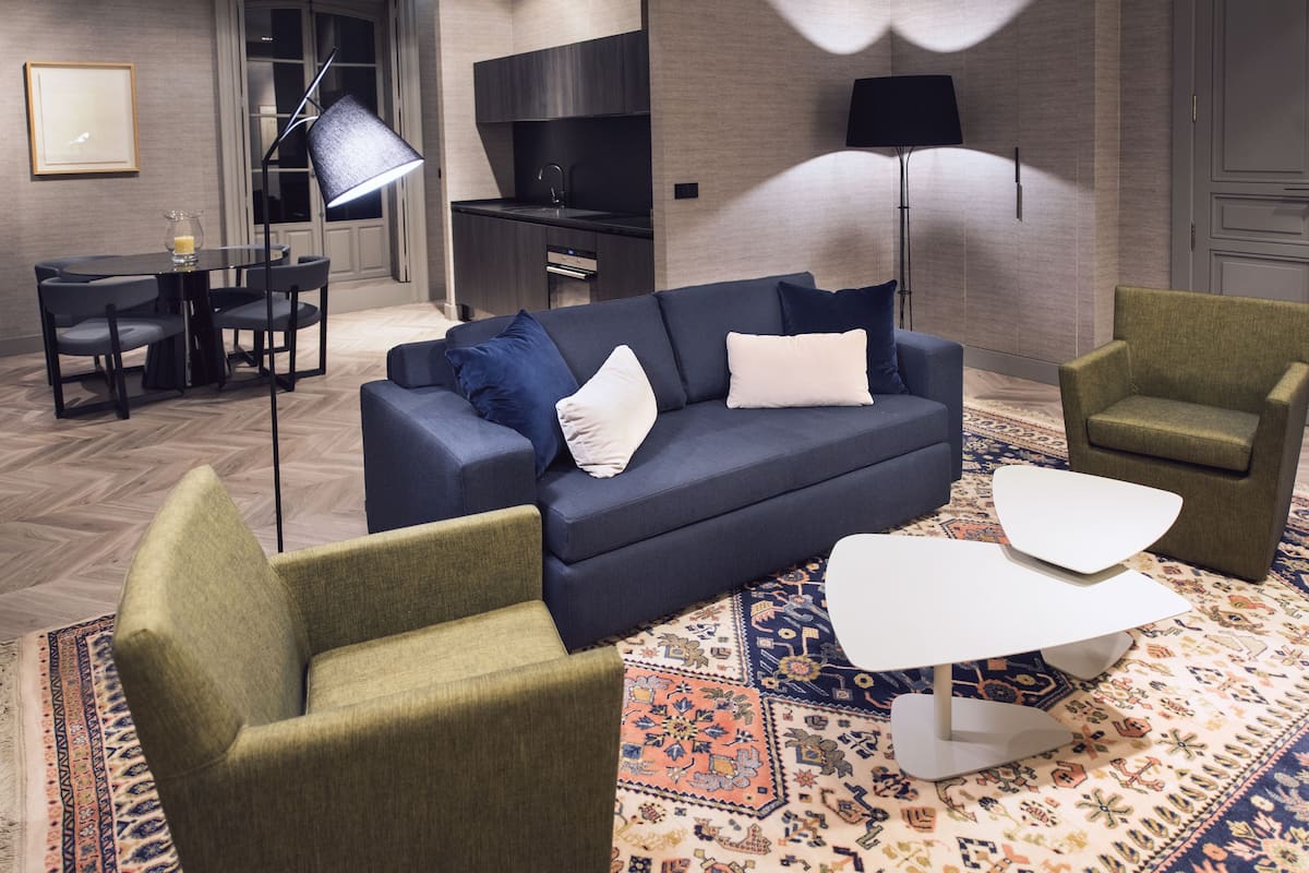 A modern living room with a dark blue sofa, green armchairs, a white coffee table, and a patterned rug.