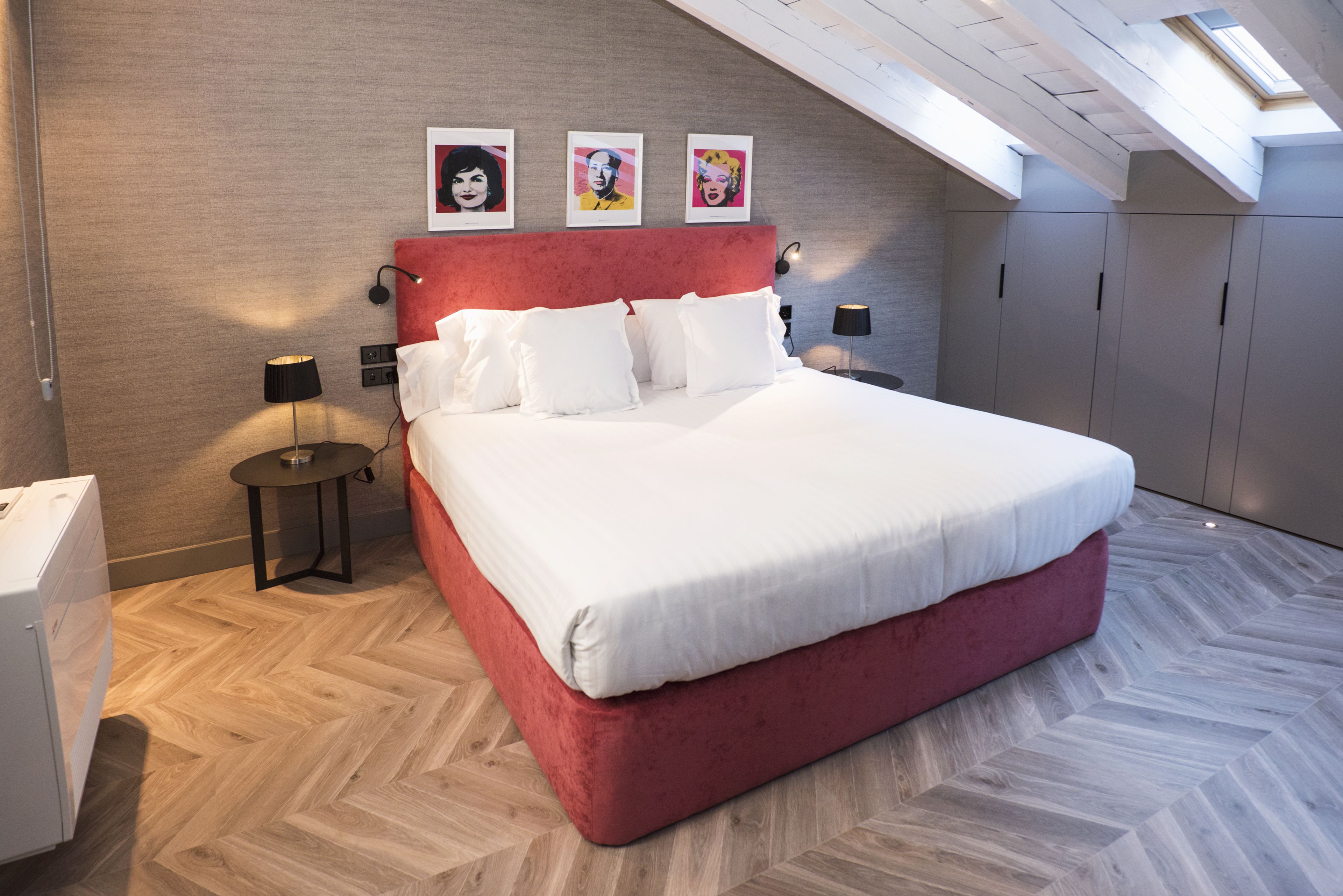 A bedroom with a large bed, a red headboard, and three framed pictures on the wall.