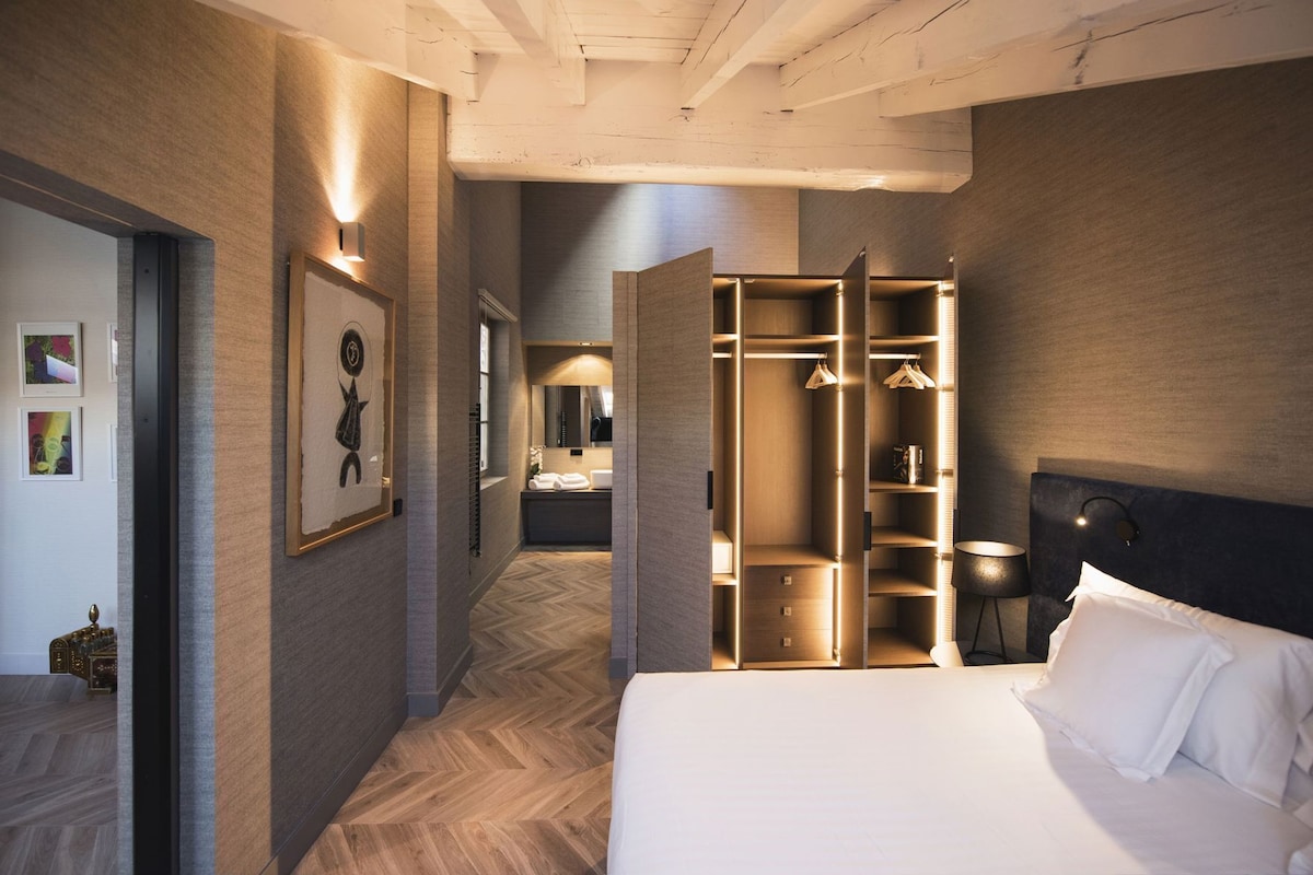 A modern hotel room with a large bed, a walk-in closet, and a hallway leading to a bathroom.