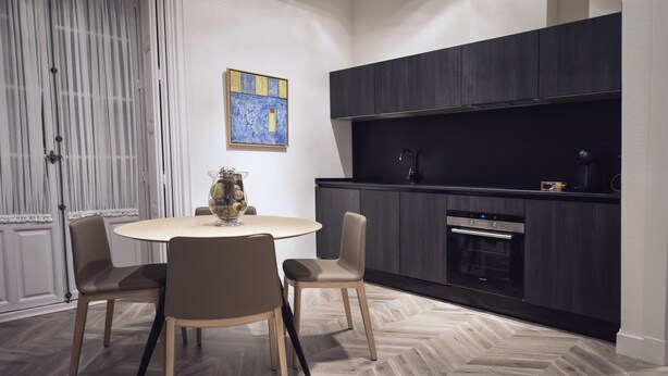 A modern kitchen with dark cabinetry, a round dining table with chairs, and a herringbone-patterned floor. - Palacio Salvetti Suites (Alicante)