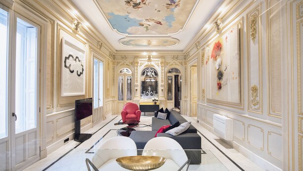 Une chambre luxueuse avec un sol en marbre, un fauteuil rouge, un canapé et une grande table blanche.
