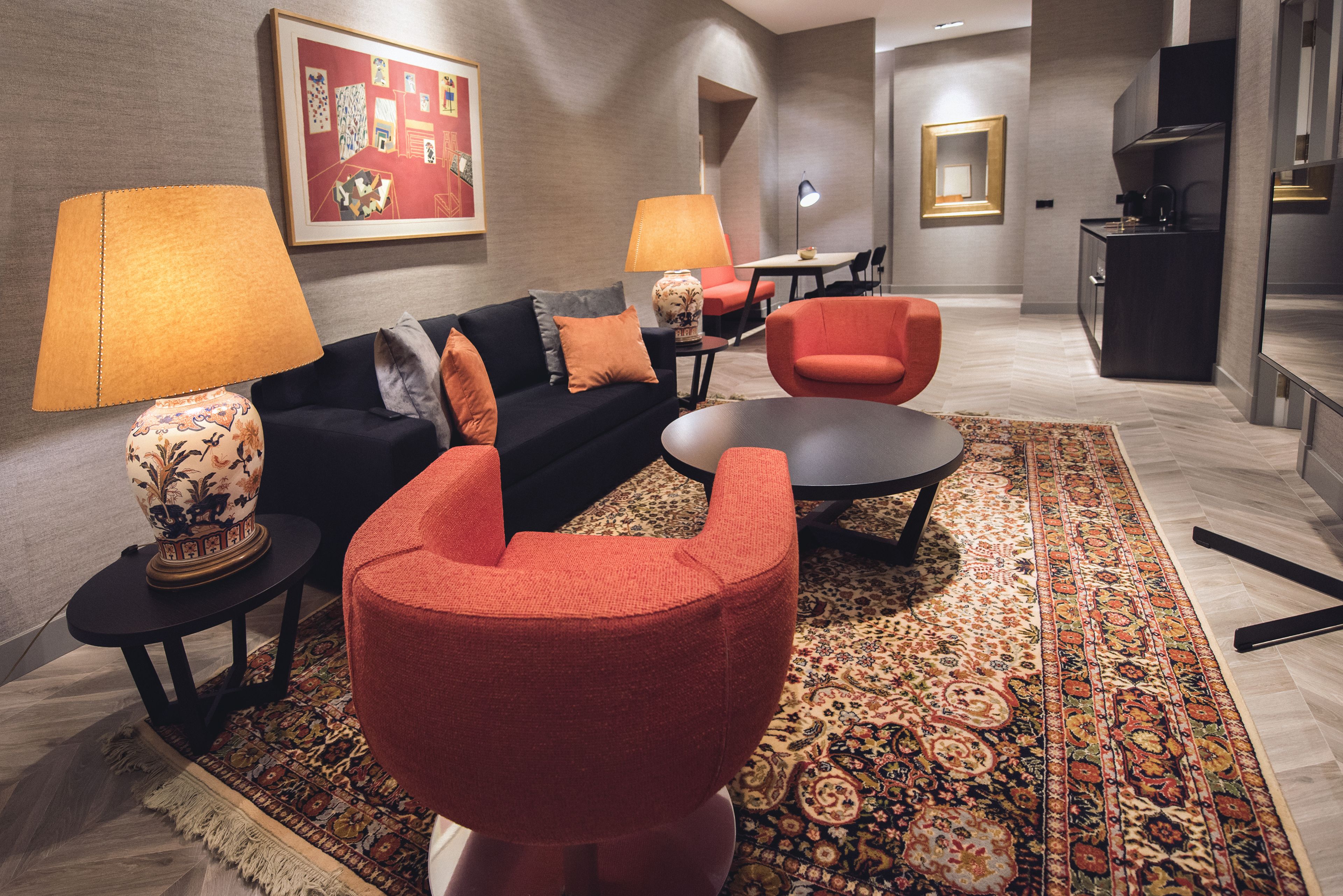 Una sala de estar moderna con un sofá, dos sillones, una mesa de centro, una alfombra estampada y una zona de comedor con una mesa y sillas.