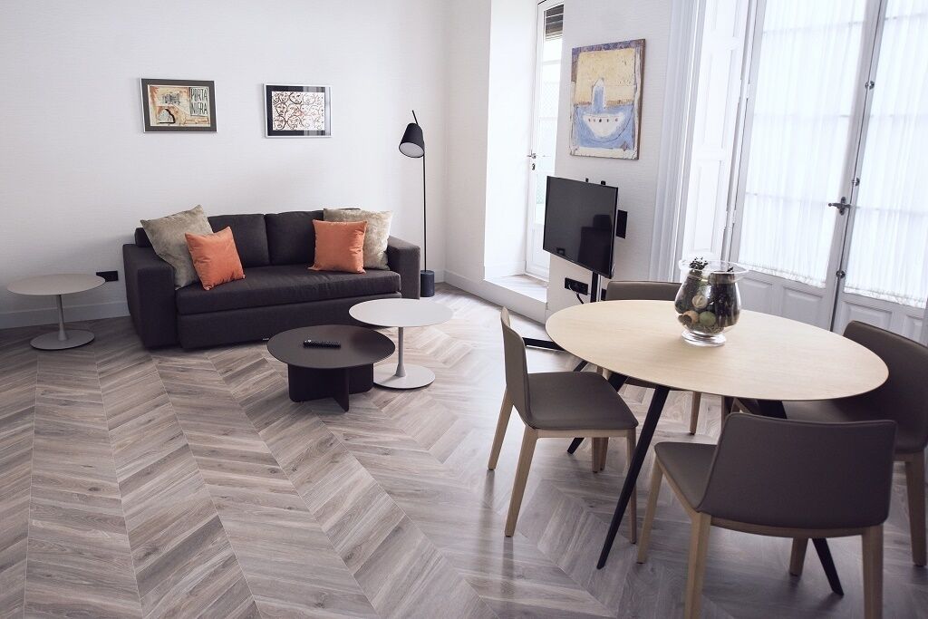 Una sala de estar moderna con un sofá, una mesa de centro y una mesa de comedor. Hay obras de arte enmarcadas en la pared, un televisor y una ventana con persianas.