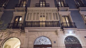 Une façade d’immeuble historique, ornée de balcons travaillés, de grandes fenêtres en arc de cercle et d’une entrée centrale agrémentée d’un portail en métal décoratif.