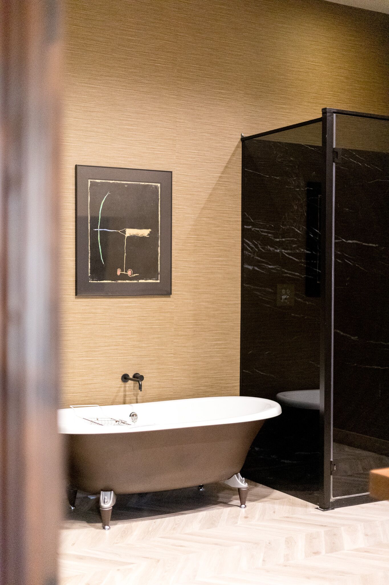 A bathroom with a freestanding bathtub, a glass shower enclosure, and a framed abstract artwork on the wall.