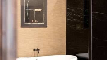 A bathroom with a freestanding bathtub, a glass shower enclosure, and a framed abstract artwork on the wall.