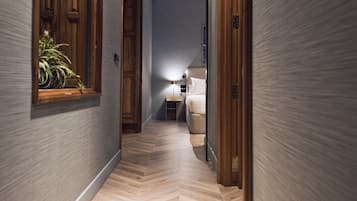 A hallway with wooden paneling, a potted plant, a bedside lamp, and a bed with white bedding.
