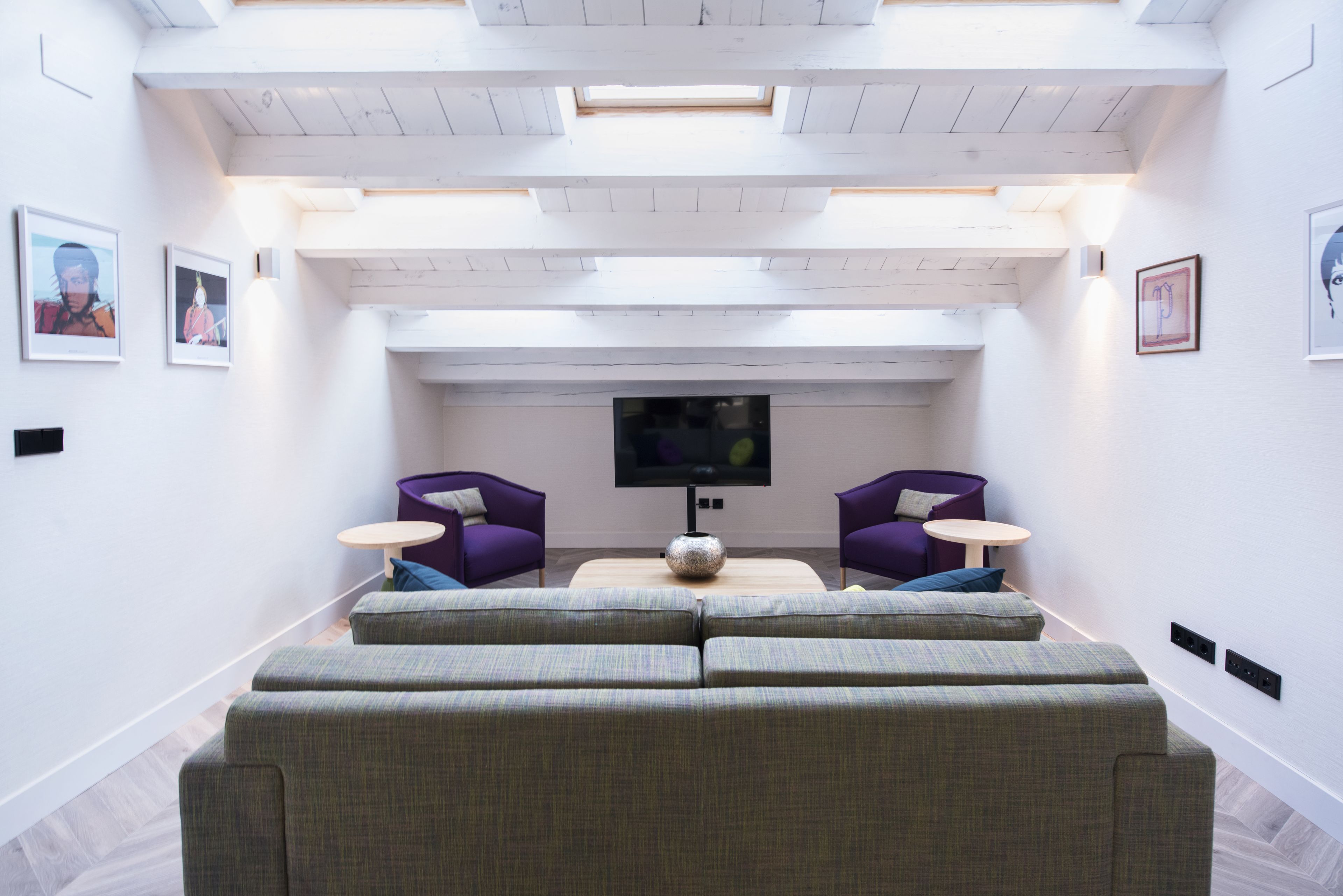 Een moderne woonkamer met een grote hoekbank, twee paarse fauteuilstoelen, een klein rond tafeltje en een flatscreen televisie.