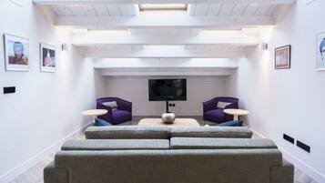 Een moderne woonkamer met een grote hoekbank, twee paarse fauteuilstoelen, een klein rond tafeltje en een flatscreen televisie.