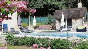 A pool area with lounge chairs, a stone building, and a garden with pink flowers. - Le Moulin de Bénédicty (Saint Gery-Vers)