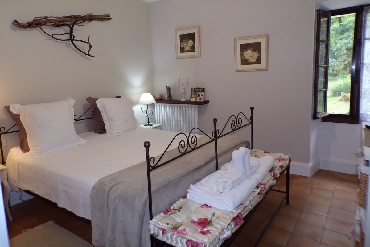 Un dormitorio con cama, mesita de noche, lámpara y ventana con vista a zonas verdes.