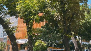 Um edifício moderno de vários andares com um design arquitetônico curvo e singular, cercado por árvores verdes e exuberantes.