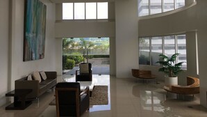 Ampla sala de estar com sofá moderno, uma mesa de centro e uma pintura grande na parede. Há duas poltronas e um vaso com planta.