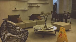 Um lobby moderno com um sofá, cadeiras, uma mesa de centro e um aviso de chão molhado.