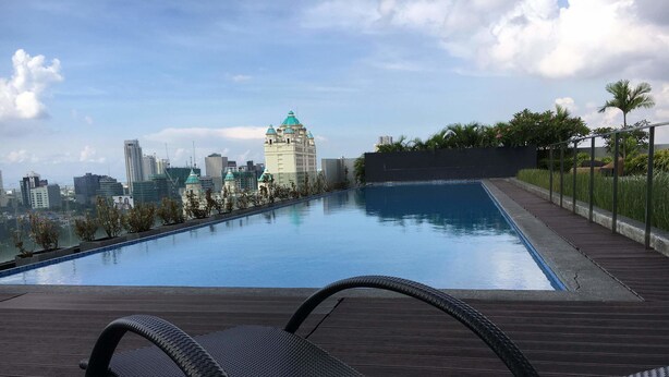 Piscina no terraço com espreguiçadeiras, vista para o horizonte urbano e um edifício com cúpula verde.