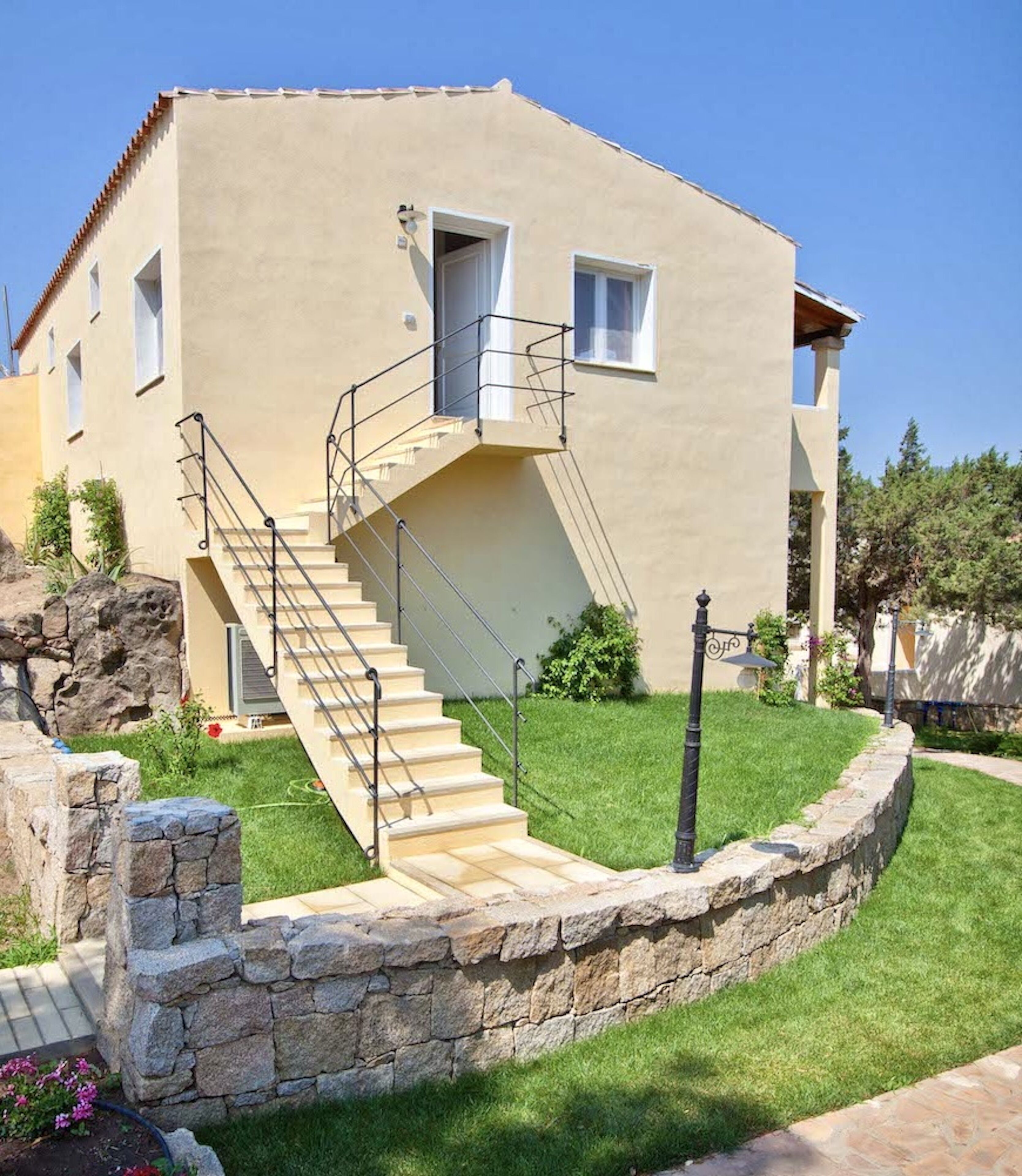 A two-story building with a stone retaining wall, a staircase with metal railings, and a well-maintained lawn.