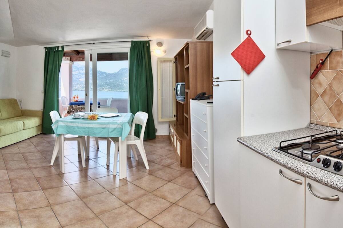 Una cocina compacta con estufa a gas, un comedor con mesa y sillas, un sofá verde y vistas al mar a través de una ventana.