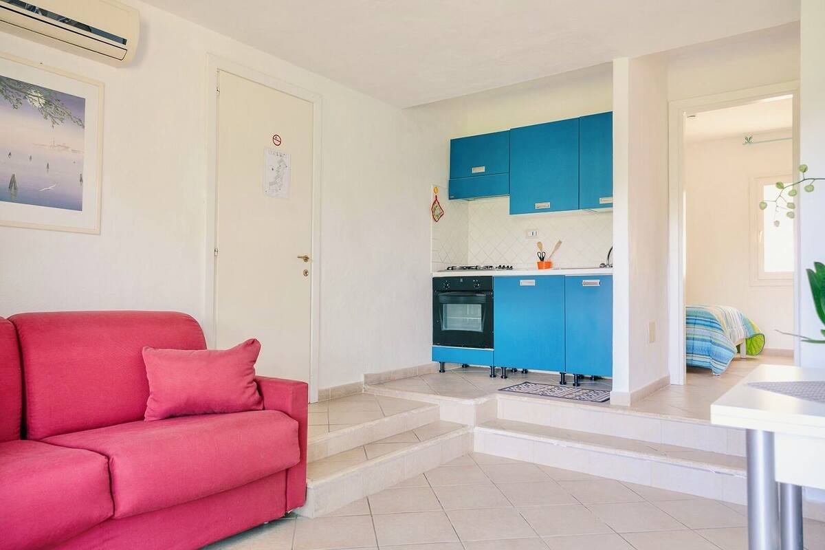 Un espacio habitable compacto con un sofá rojo, una kitchenette con armarios azules y una pequeña zona de comedor.