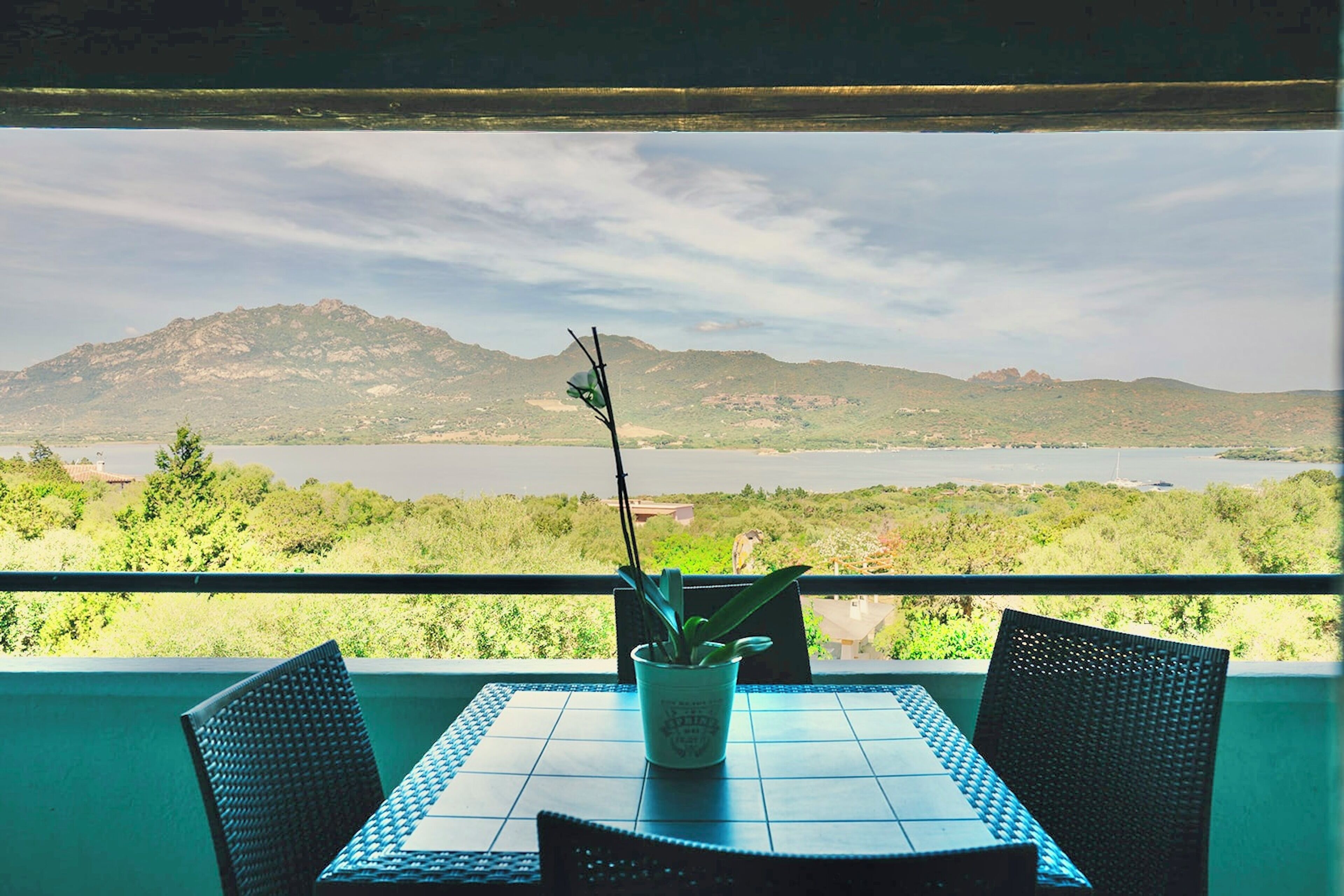 Un balcon avec une table et des chaises, un pot de fleurs et une vue sur une montagne et un lac.