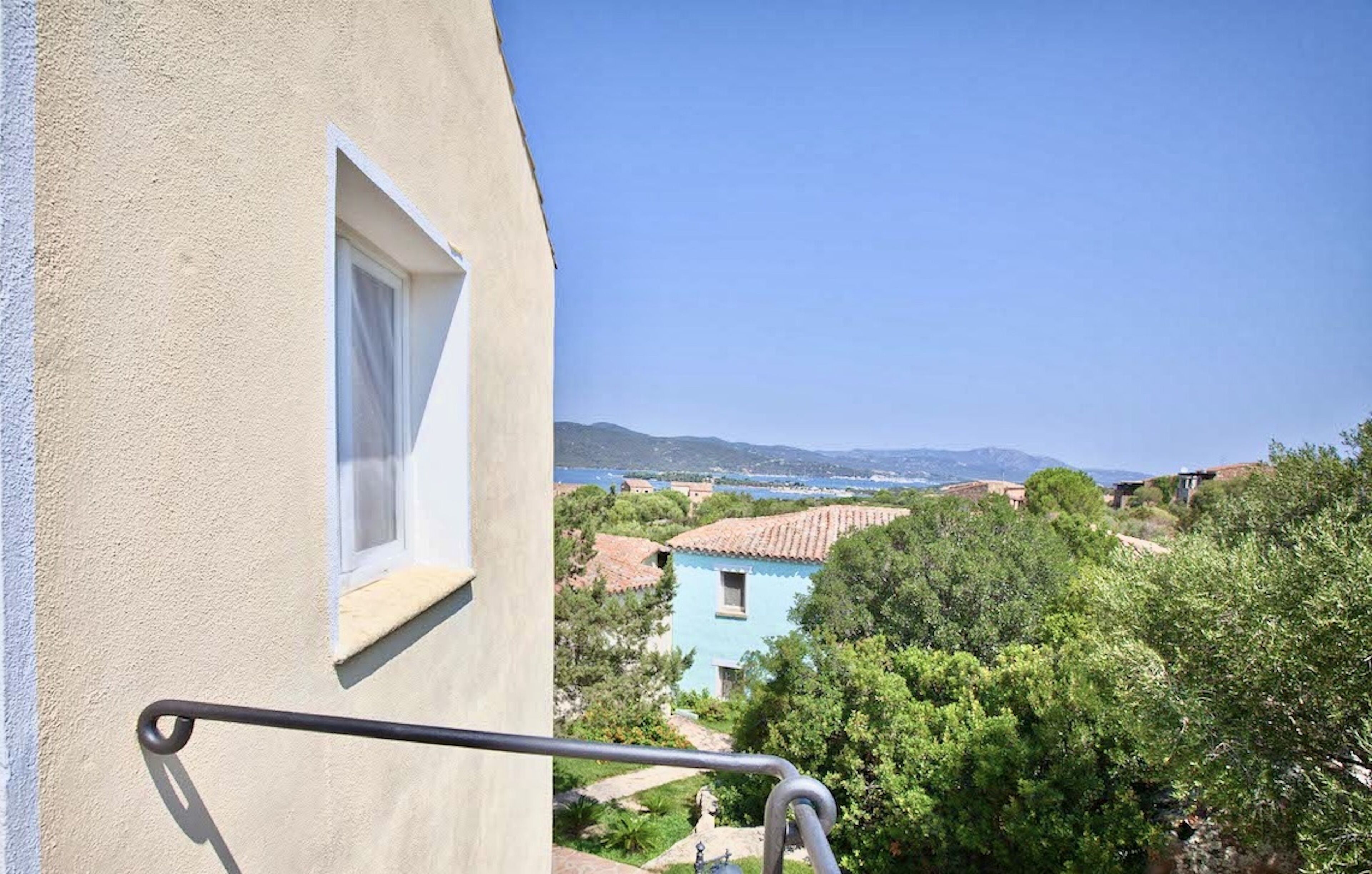 A balcony with a view of a coastal village, including houses and a clear blue sky.