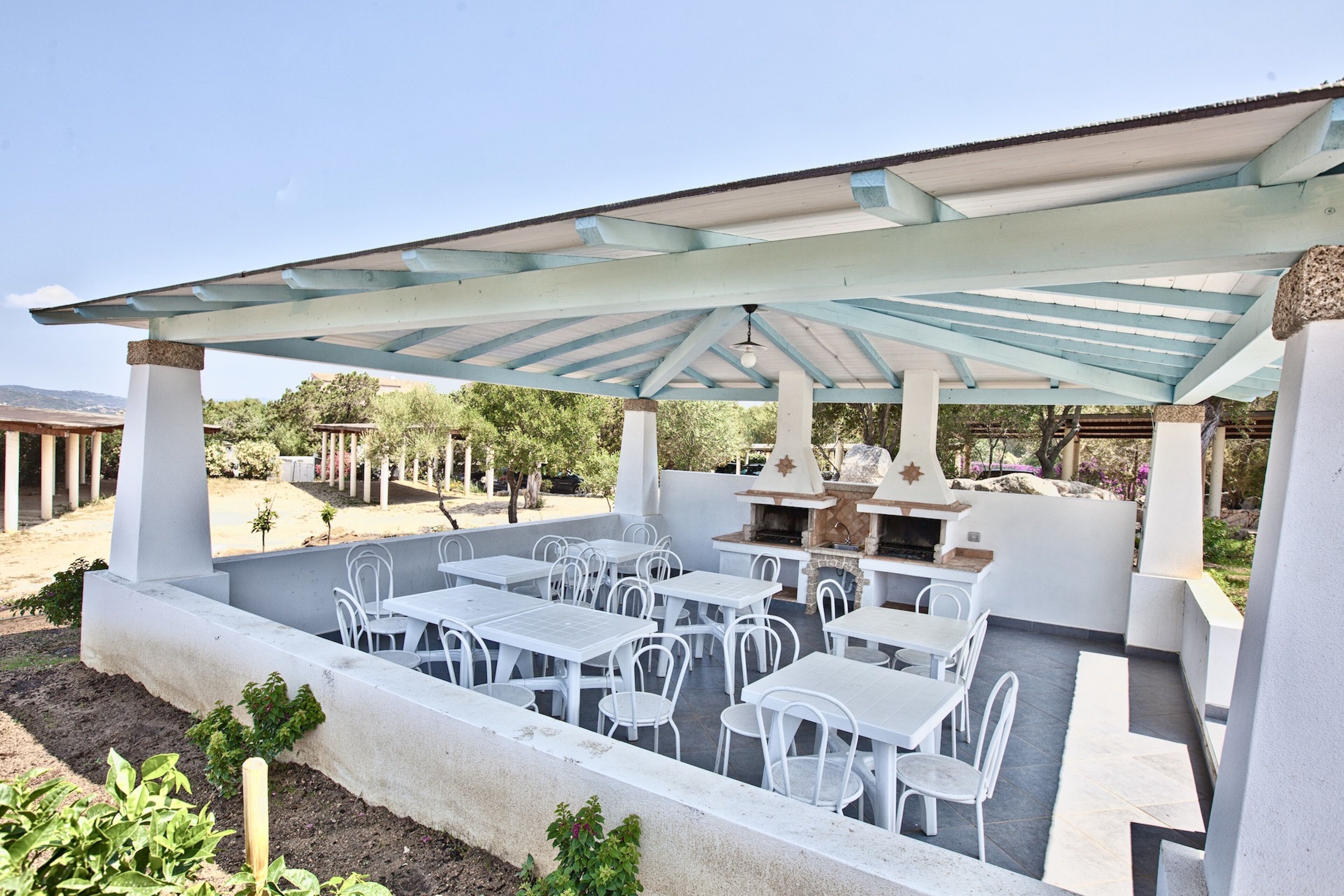 Une terrasse extérieure avec des tables et des chaises blanches, un espace salon couvert et un barbecue.