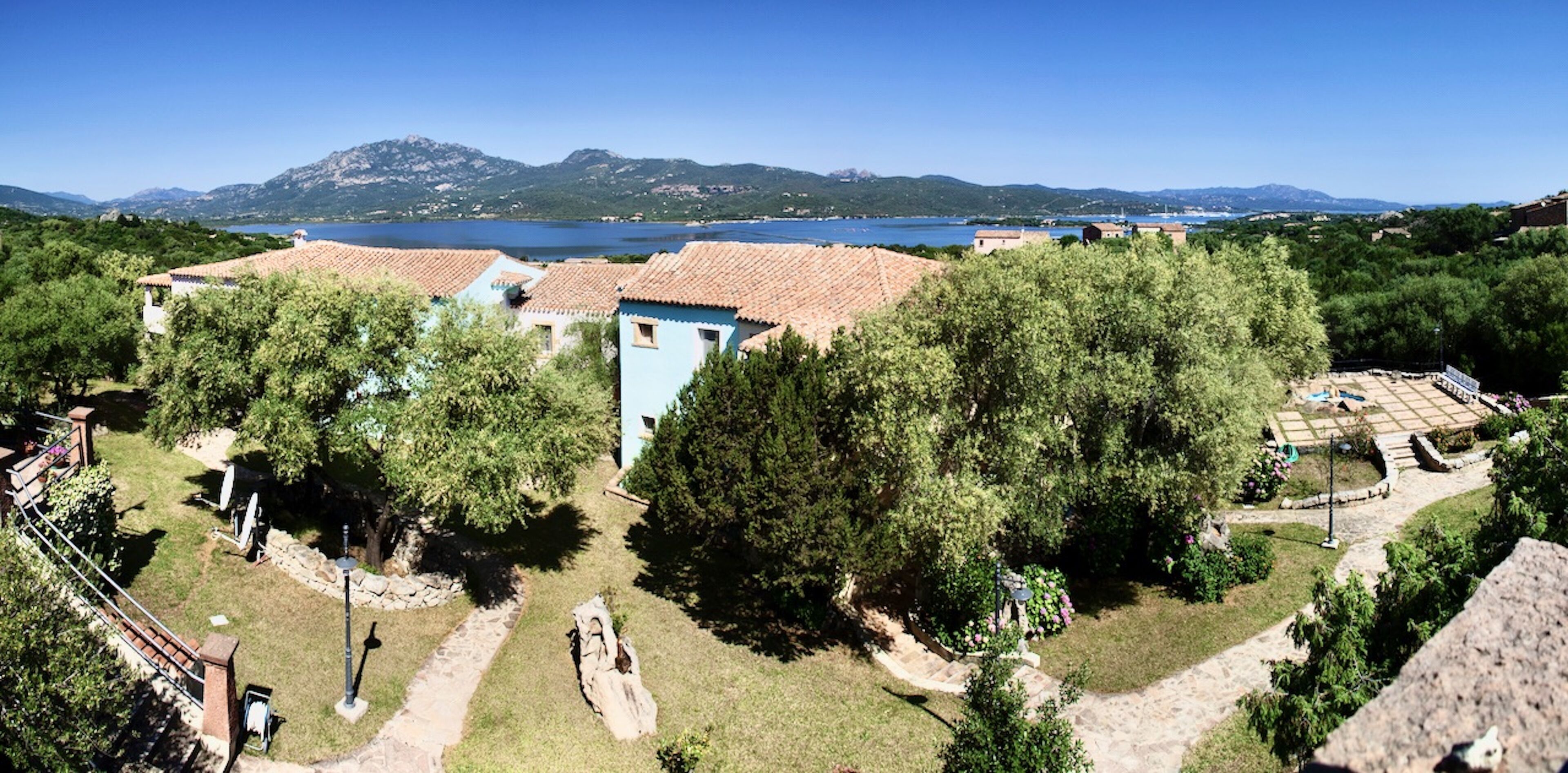 A coastal villa with terracotta roofs, surrounded by lush greenery and a view of the sea.