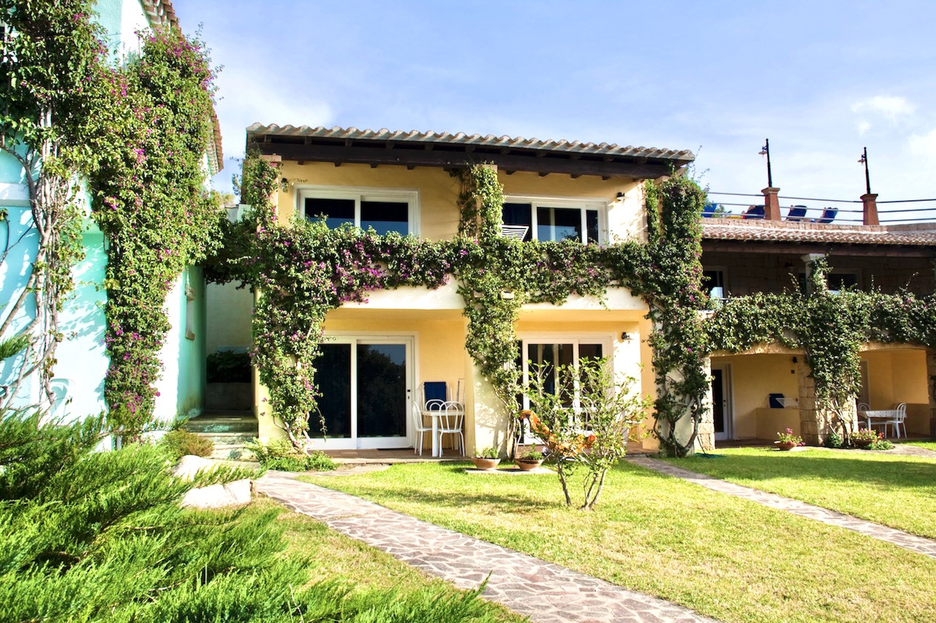A two-story house with a covered patio area, a small garden, and a pathway leading to the entrance.