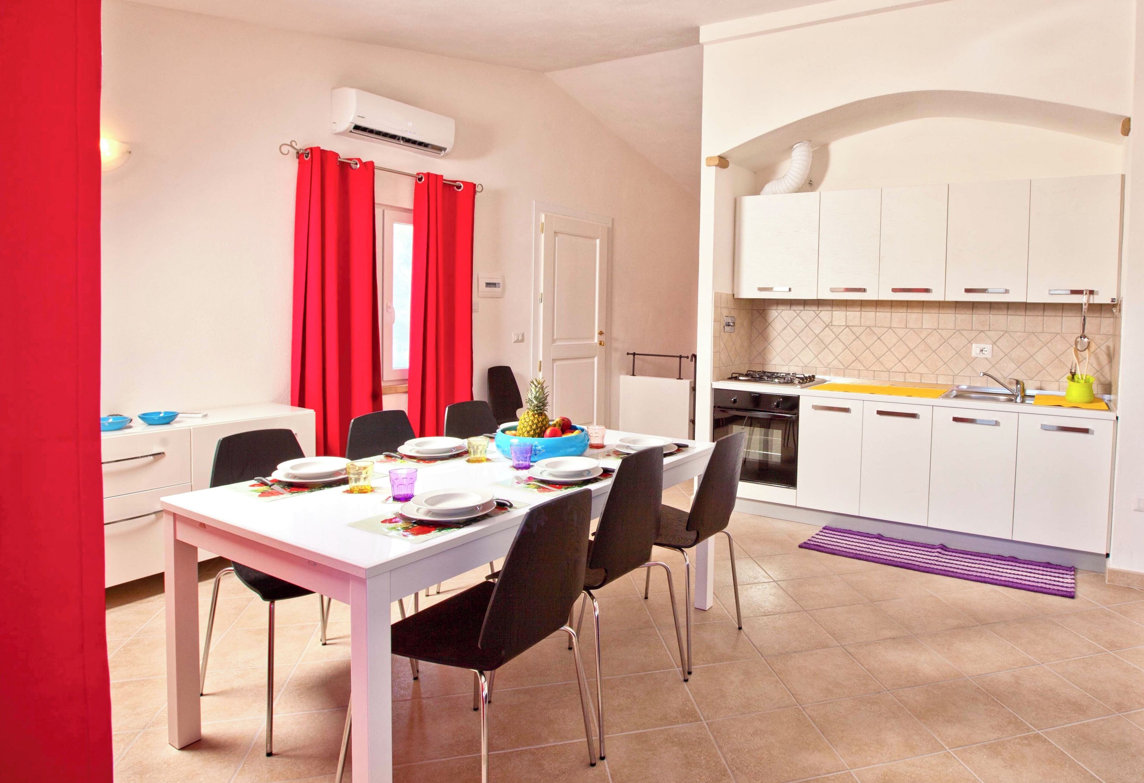 Une cuisine moderne avec des meubles blancs, une cuisinière et un coin repas comprenant une table blanche et des chaises noires.