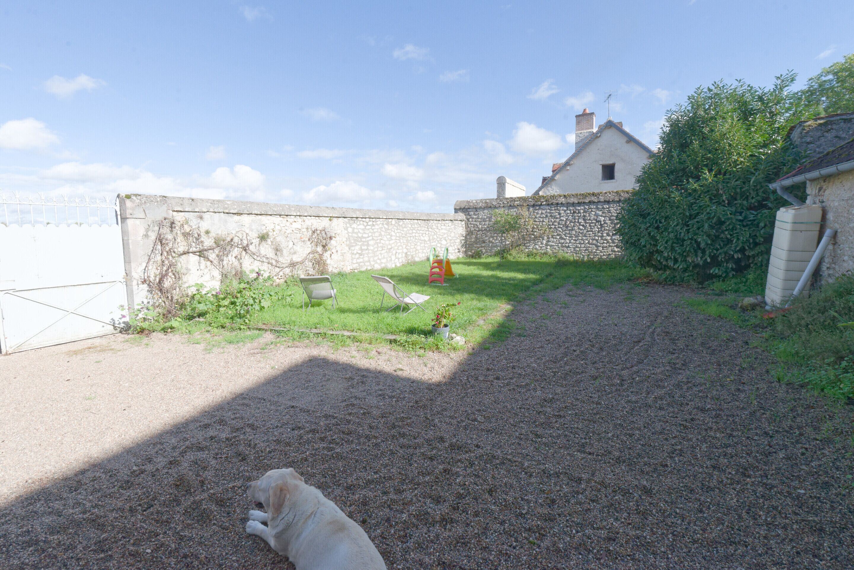 A gravel path leading to a stone wall with a grassy area and a white building with a chimney.