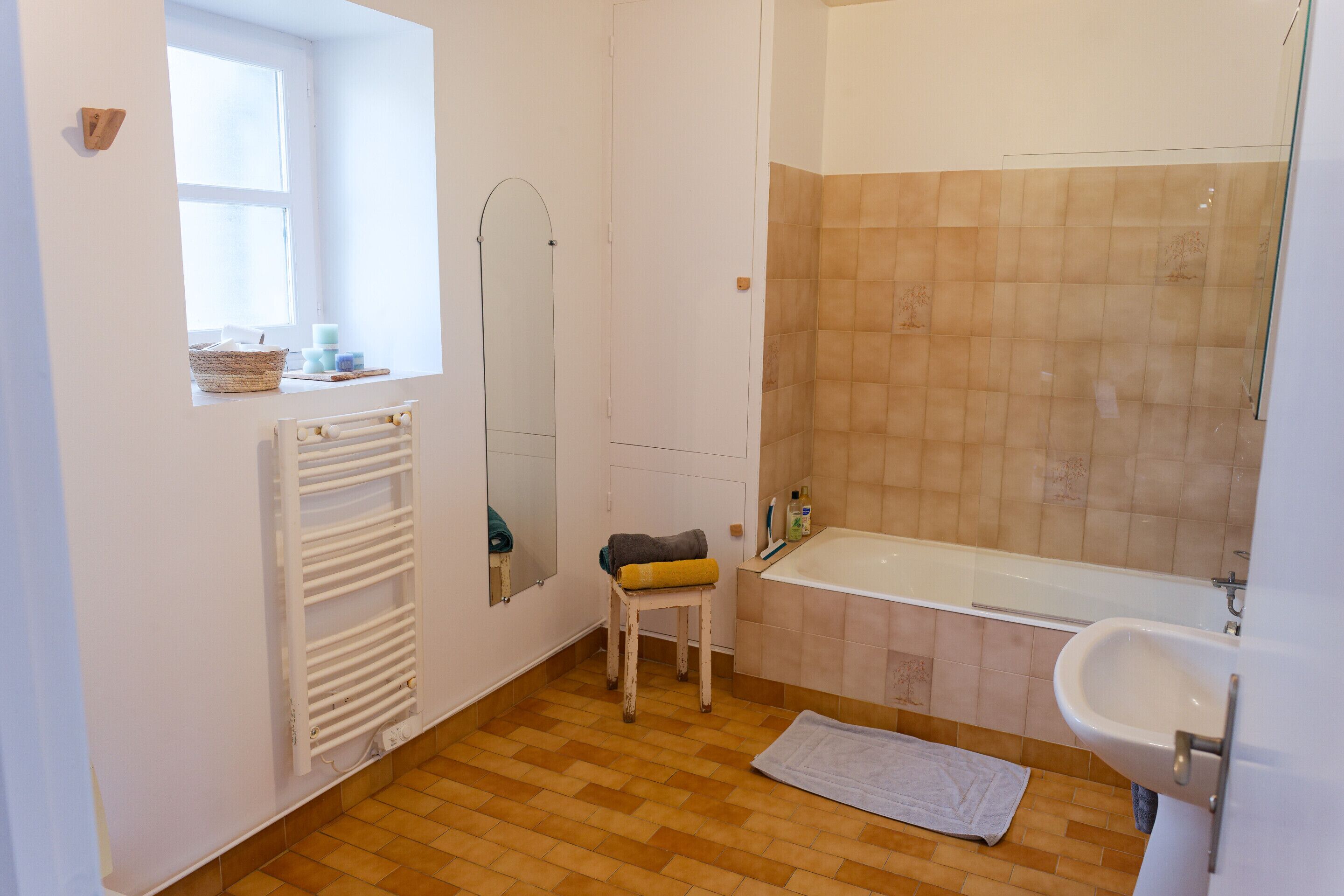 Une salle de bain avec une baignoire, un lavabo, un miroir, un radiateur et une fenêtre.
