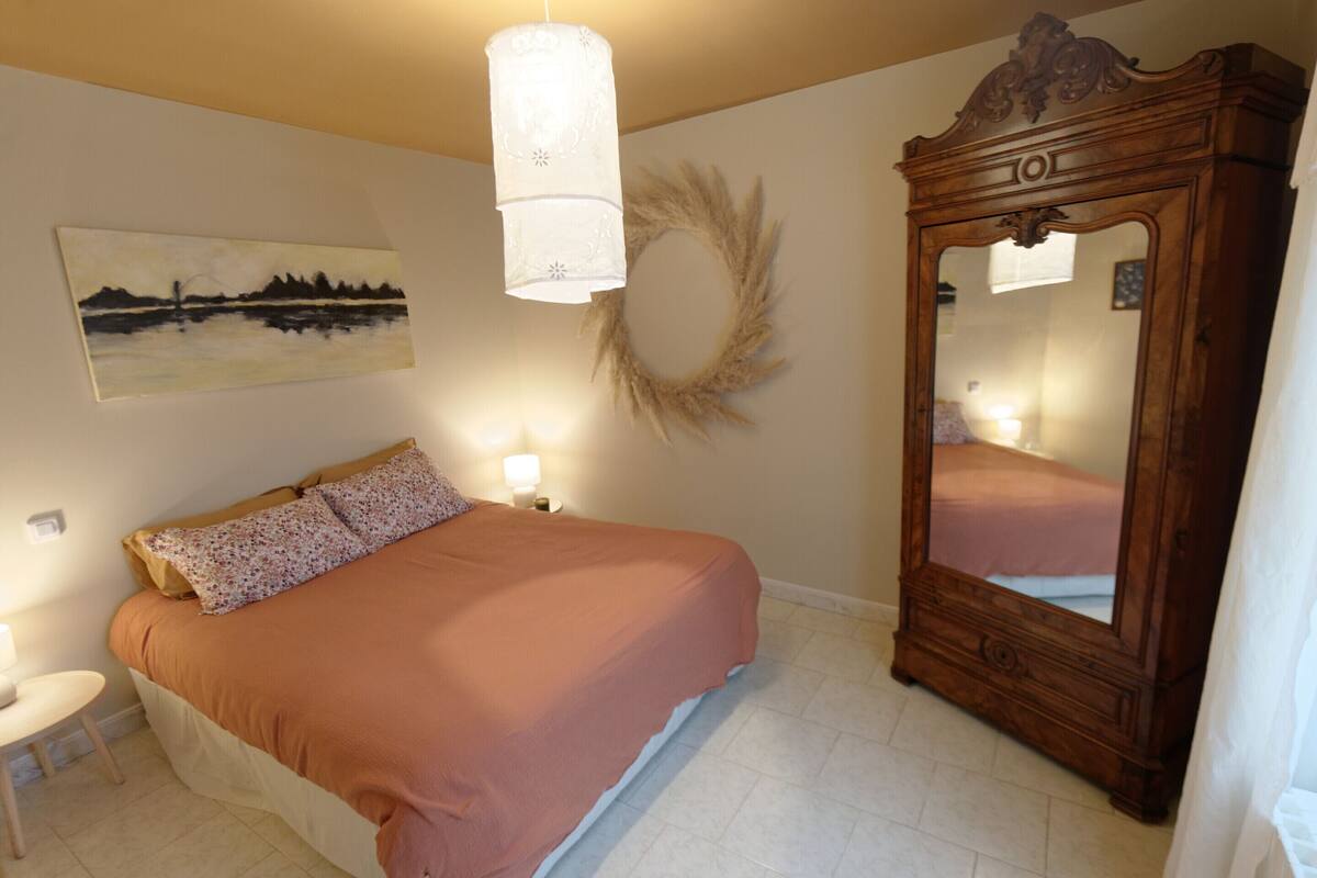 Une chambre à coucher avec un lit, des lampes de chevet, un grand miroir et une œuvre d’art accrochée au mur.