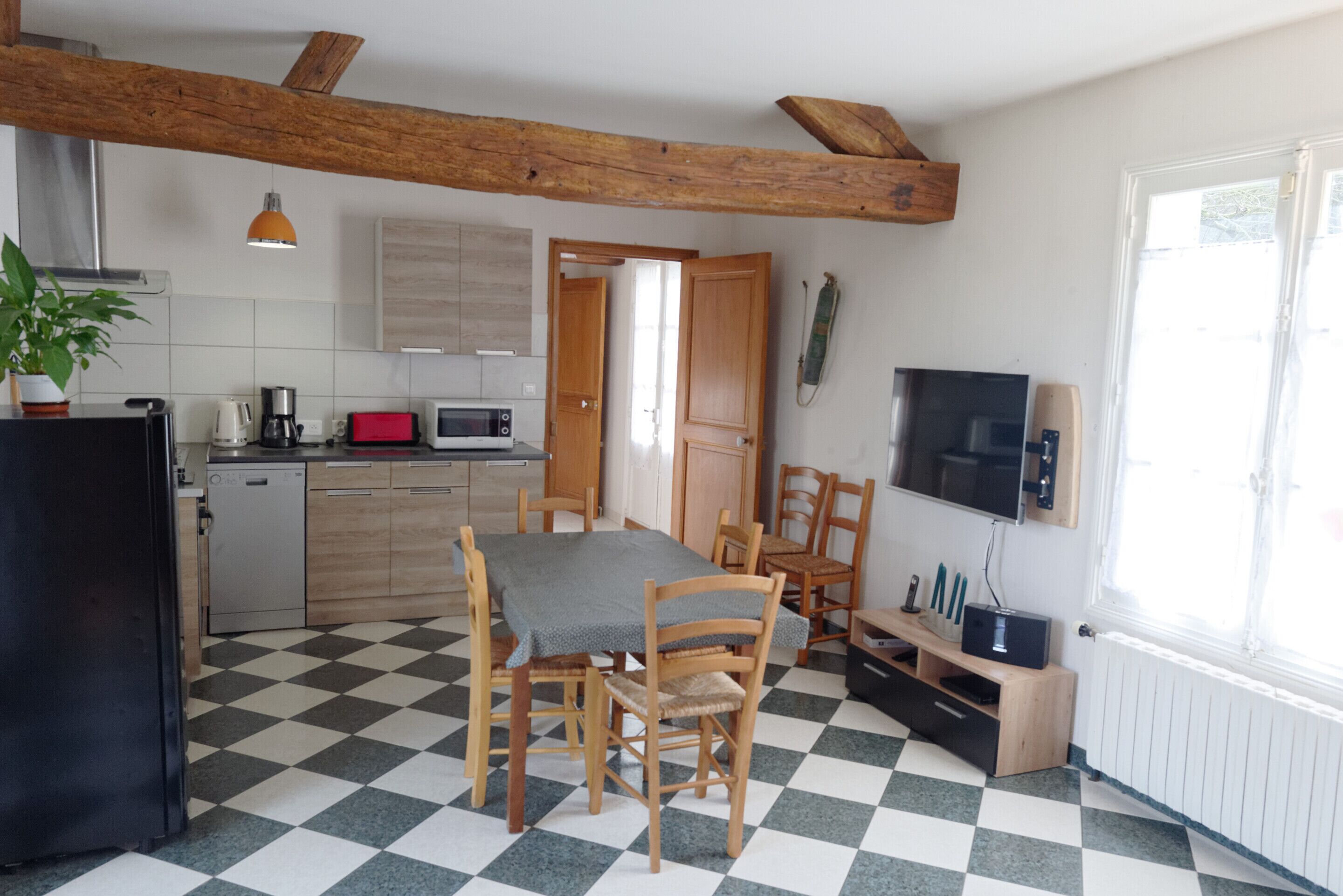 A compact kitchen with a dining area, featuring a checkered floor, wooden furniture, and basic appliances.