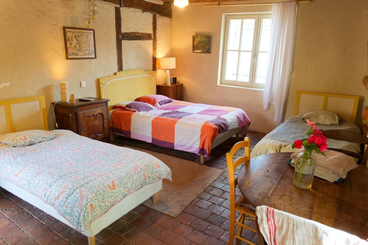 Une chambre confortable avec deux lits, une table en bois ornée d’un vase de fleurs et une fenêtre avec des rideaux.