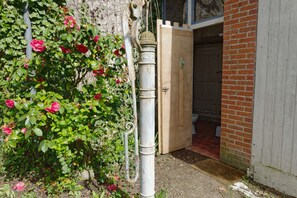 Een rustiek gebouw met een houten deur, een metalen pijp en een rozenstruik op de voorgrond.