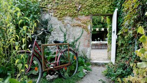 A bicycle parked in a garden path leading to a rustic brick wall with a white door.