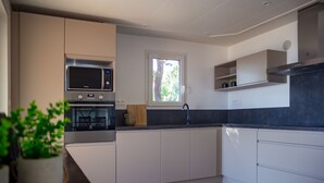 A modern kitchen with white cabinets, a microwave, and a window. - Résidence SerenAmore (Conca)