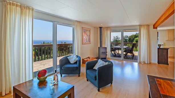A spacious living area with a large sliding glass door leading to a balcony, a dark blue sofa, a wooden coffee table, and a small TV. - Résidence SerenAmore (Conca)